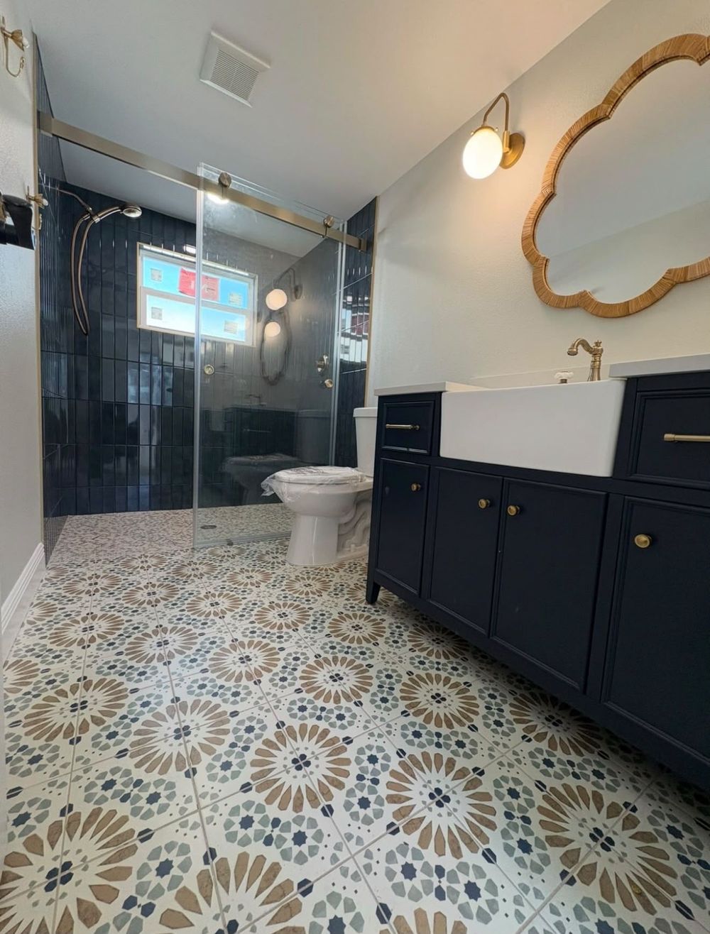 Finished bathroom with navy vertical-stack shower tile, sliding glass door, patterned floor tile and navy vanity with brass hardware